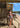Woman in a bikini standing on a wooden deck by the beach with a surfboard lesson sign in the background.