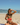 Woman in a bikini holding a watermelon slice on a beach with people in the background