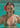 Woman in a floral bikini with a red flower in her hair, standing in clear blue water.