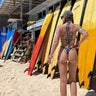 Person in a bikini standing next to surfboards on a beach