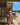 Woman in a bikini standing on a wooden deck by the beach with a surfboard lesson sign in the background.
