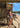 Woman in a bikini standing on a wooden deck by the beach with a surfboard lesson sign in the background.