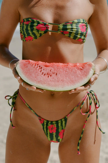 Woman in a colorful bikini holding a watermelon slice on a beach.