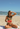 Woman in a bikini holding a watermelon slice on a beach with people in the background