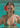 Woman in a floral bikini with a red flower in her hair, standing in clear blue water.